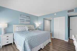 A bedroom with a bed, nightstands, a wall-mounted lamp, a painting, a closet, and a door.