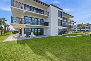 A modern multi-story building with balconies, outdoor seating, and a well-maintained lawn.