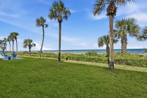A grassy area with palm trees and a view of the ocean. - Perfect Beachfront Escape at Ocean House 122 (St. Augustine)