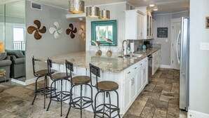 Een moderne keuken met een centraal eiland, barkrukken, hanglampen en decoratieve wandkunst.