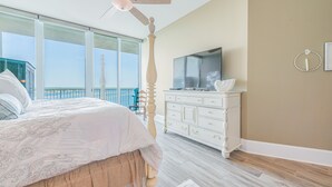 A bedroom with a bed, a television, a dresser, and a balcony with a view.