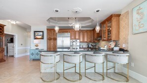 A spacious kitchen with a central island, bar stools, a refrigerator, and pendant lighting.