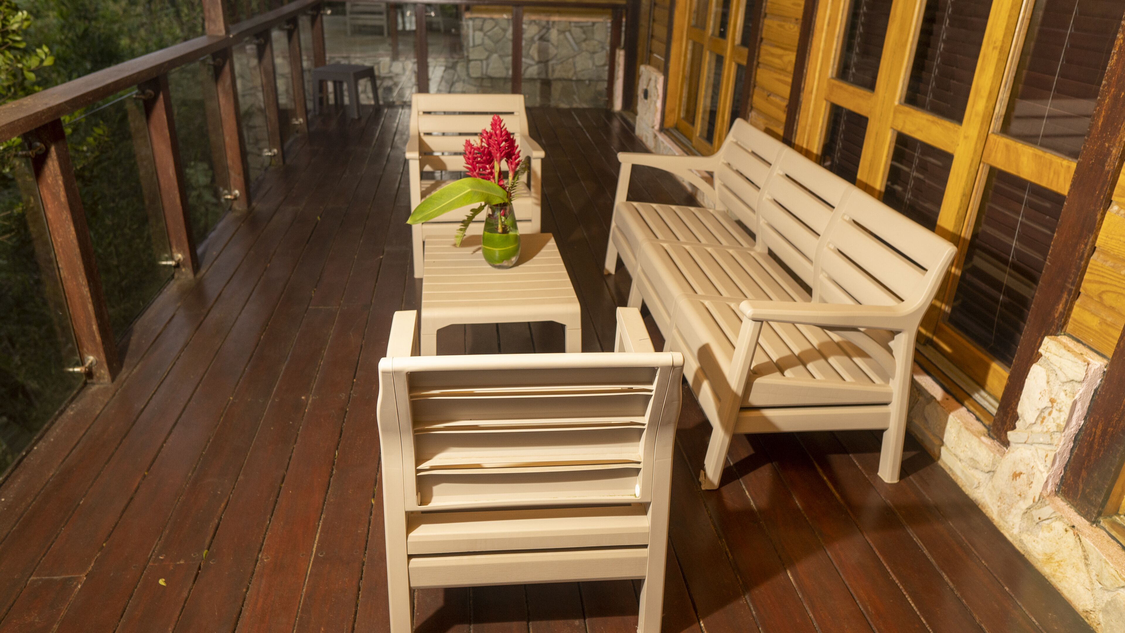 A wooden deck with white furniture, including a bench and a table with a vase of flowers.