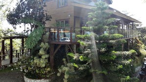 A wooden house with a glass bridge and a car parked in front. - Loma de Sion (San Francisco de Macorís)