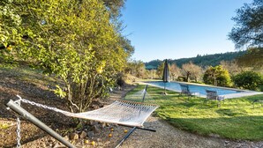 A hammock on a gravel path, a pool, and a grassy area with trees.
