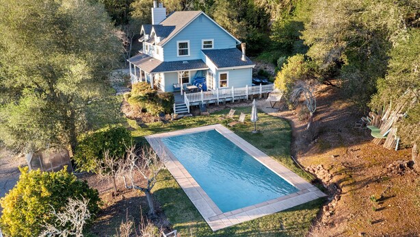 A two-story house with a swimming pool, surrounded by trees and a fenced yard.
