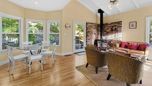 A spacious living room with a fireplace, large windows, and a dining area with white chairs.