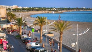A beachside promenade with parked cars, palm trees, and a clear view of the sea.
