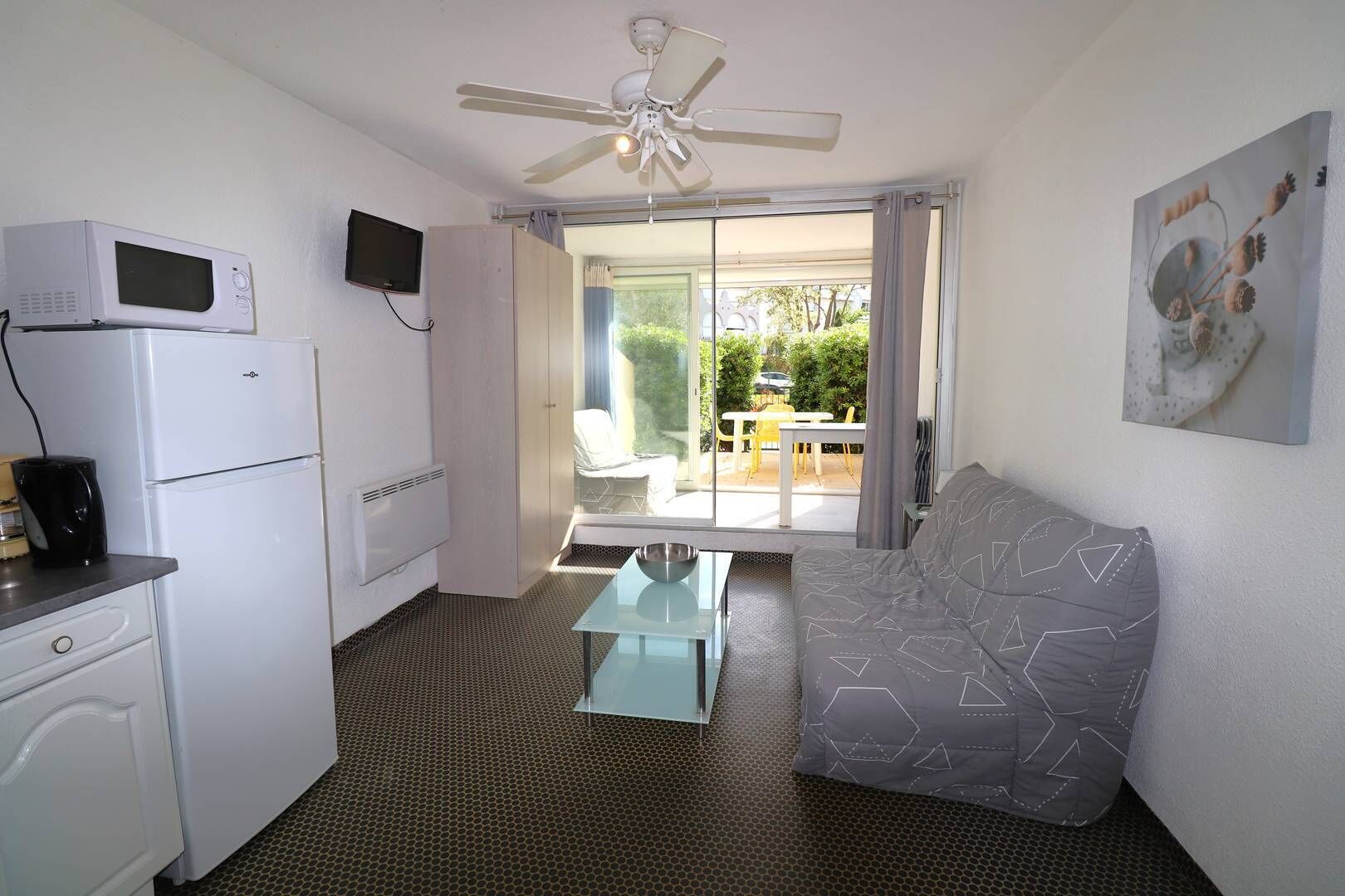 A compact room with a kitchenette, a ceiling fan, a sofa, and a dining area with a view of the outdoors.