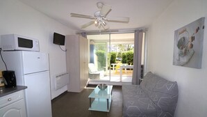 A compact room with a kitchenette, a ceiling fan, a sofa, and a dining area with a view of the outdoors.