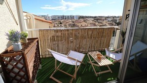 Un balcone con vista sulla città, una sedia di legno, un tavolino e una pianta in vaso.