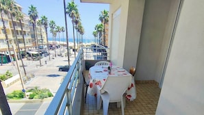 A balcony with a tiled floor, a table with a floral tablecloth, and a chair. - 2-Bedroom Apartment Close to the Beach, Shops, Entertainment  5CDUSUD1 (CANET PLAGE)