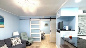 Una sala de estar moderna con un sofá, una mesa de centro, un televisor y una cocina con mostrador y taburetes.
