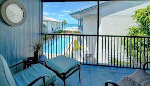 A balcony with a view of a pool and ocean, a clock, and a chair.