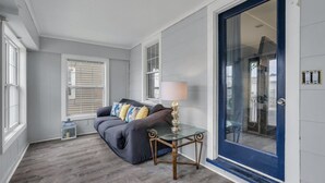 A room with a grey sofa, a glass table with a lamp, and a blue door. - Beach house! Sleeps 8, off street parking (Manasquan)