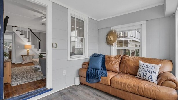 A living room with a brown leather sofa, a blue throw blanket, and a pillow with text. There is a staircase leading to another room, a lamp, and a wall-mounted wreath. - Beach house! Sleeps 8, off street parking (Manasquan)