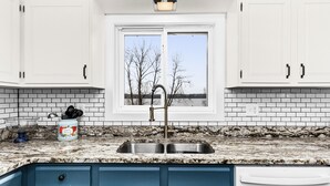 A kitchen with white cabinets, a granite countertop, and a window with a view of trees and a body of water.
