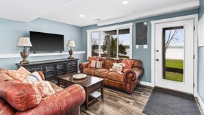 A living room with a brown leather sofa, a coffee table, and a flat-screen TV mounted on the wall.