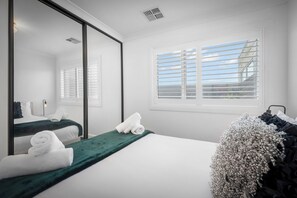 Relax in a serene space with a large bed, full-length mirror, and natural light pouring in through the window.