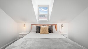 A bedroom with a sloped ceiling, a skylight, a bed with a grey blanket, two bedside tables with lamps, and a wooden headboard. - Brisbane Terrace - Hobart Inner City - Free Parking - Free WIFI (Hobart)