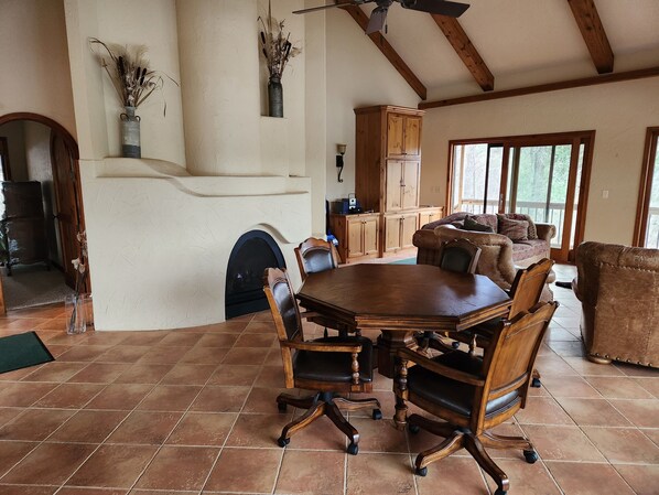 A dining area with a large wooden table, six chairs, and a fireplace. There is a wooden cabinet and a sofa in the background.
