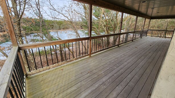Une terrasse en bois avec une rambarde en métal, donnant sur une étendue d’eau et des arbres.