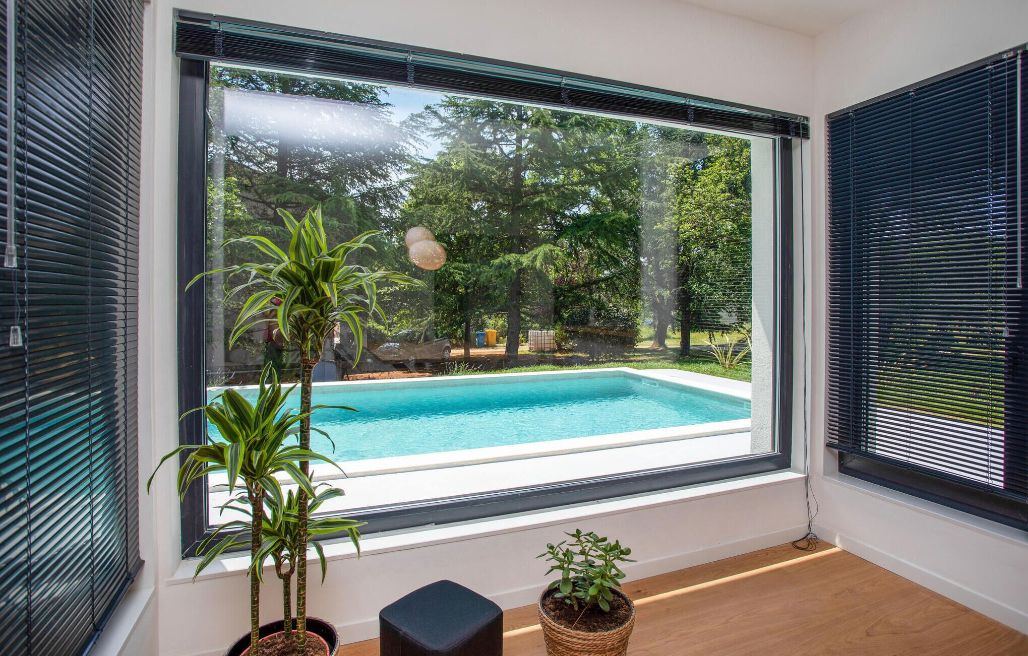 A room with a large window overlooking a swimming pool and lush greenery.