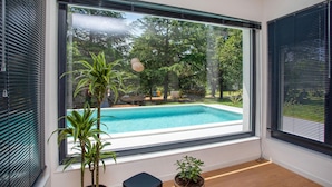 Ein Zimmer mit großem Fenster mit Blick auf ein Schwimmbad und üppige Grünflächen.