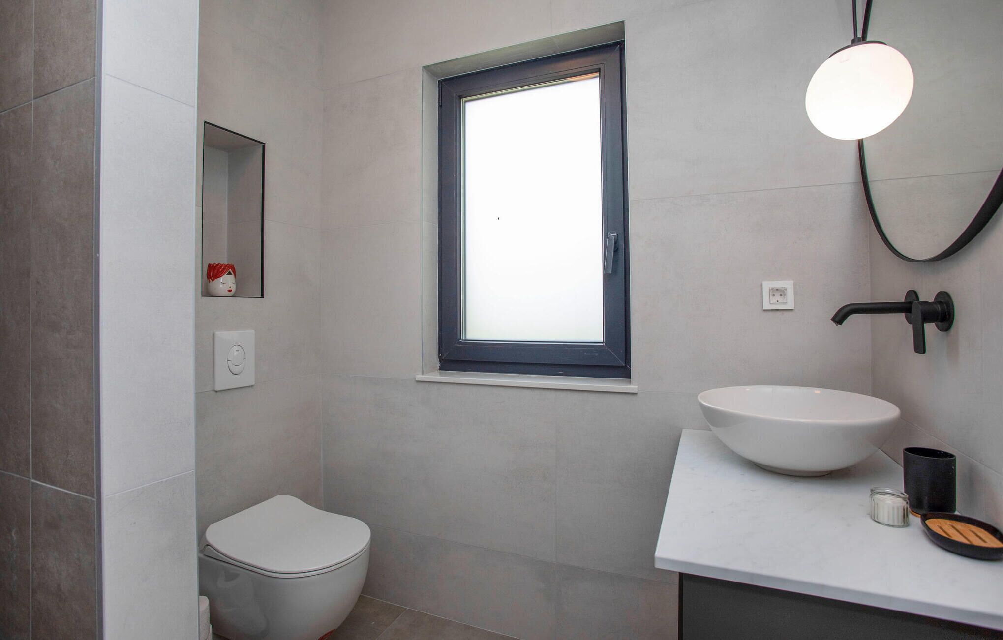 A modern bathroom with a toilet, a window, a sink, and a mirror.