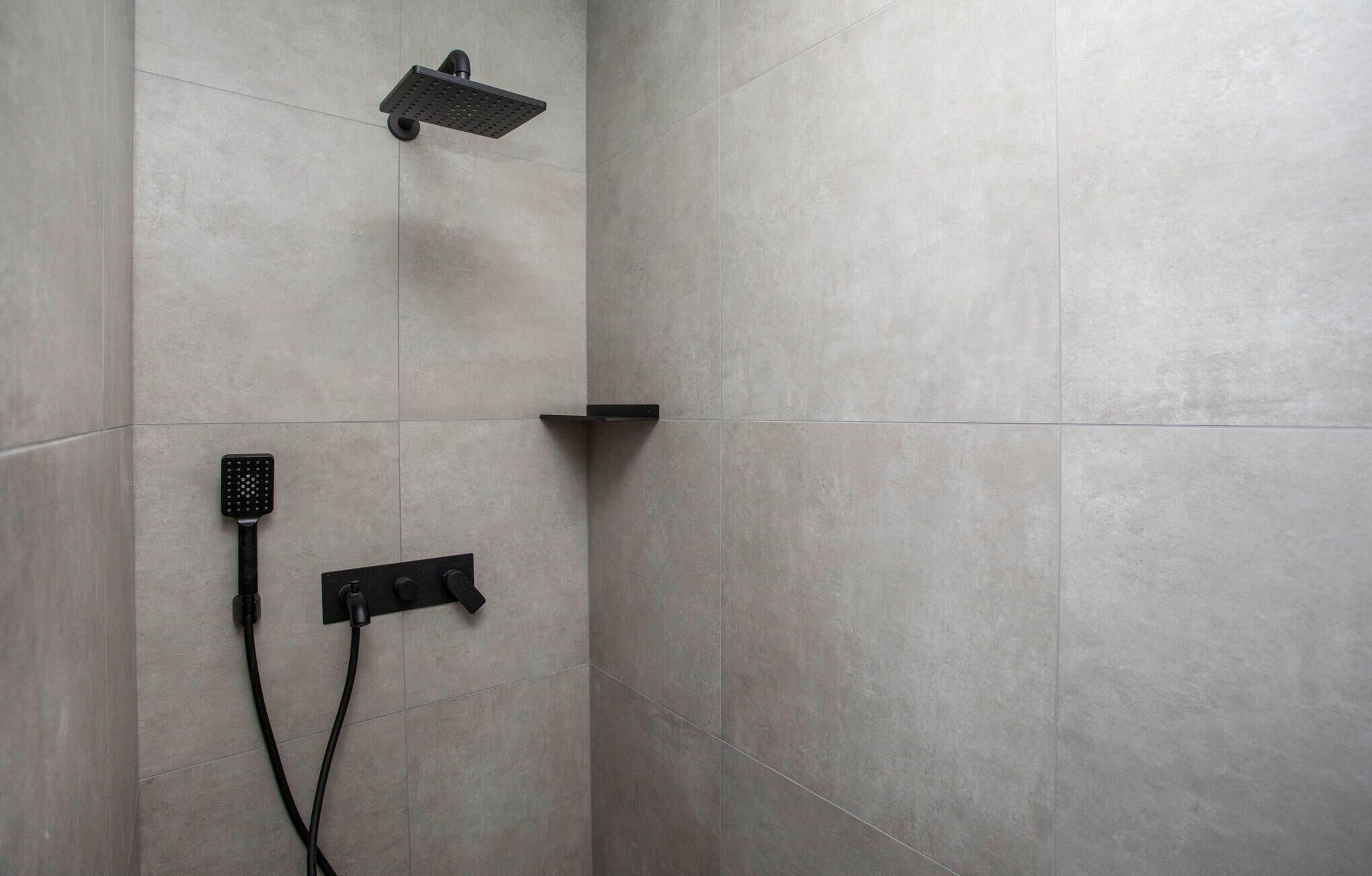 A shower area with a handheld showerhead and a wall-mounted control panel.