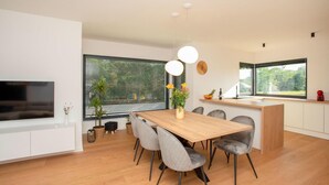 Eine moderne Küche mit einer Holzinsel, einem Essbereich mit großem Tisch und Stühlen sowie einem an der Wand montierten Fernseher.