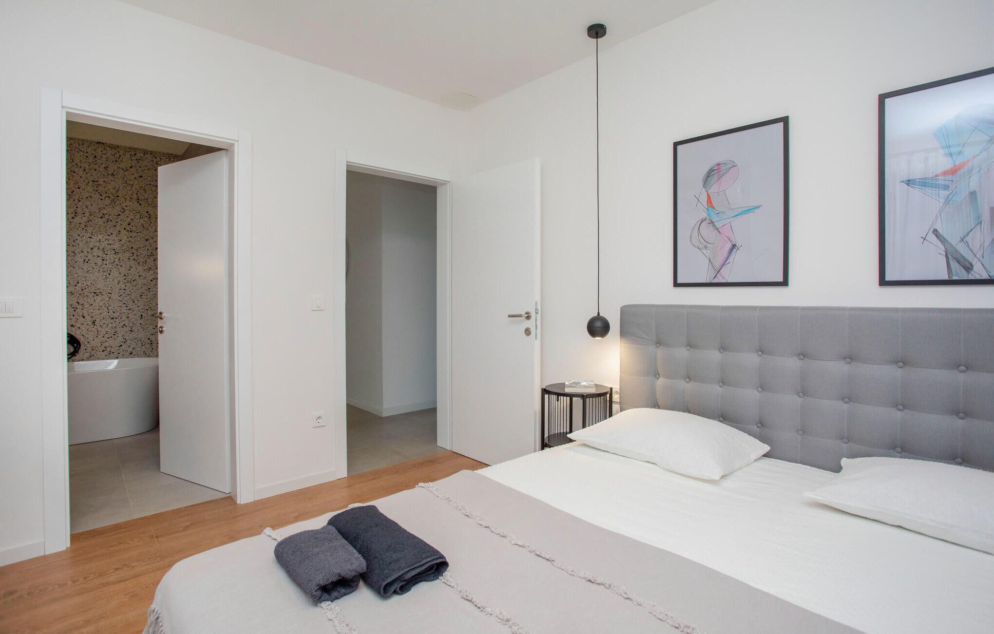 A modern bedroom with a grey tufted headboard, white bedding, and two abstract paintings on the wall.