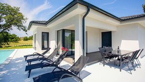 Ein modernes Haus mit Pool, Sitzgelegenheiten im Freien und einem Essbereich.