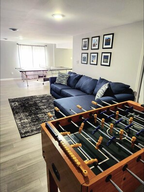 Uma sala de estar com mesa de pebolim, sofá, mesa de centro e mesa de tênis de mesa.