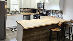 A modern kitchen with white cabinets, a wooden island, and bar stools.