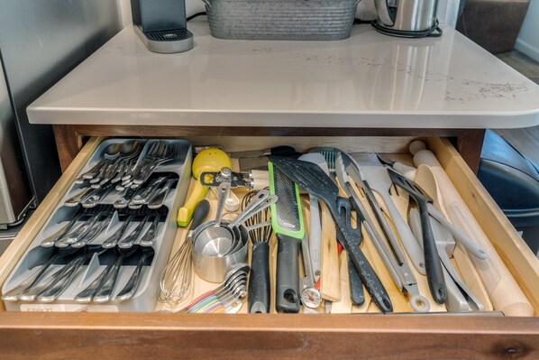A drawer with various kitchen utensils including spoons, forks, knives, and a whisk.