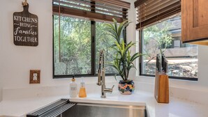 A kitchen with a stainless steel sink, wooden cabinets, a potted plant, and a window with blinds. - Casa de la Paloma -  Peaceful Golf Course Luxury Retreat (Tucson)