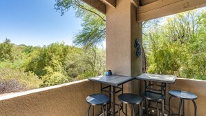 An outdoor patio with a table and four stools, surrounded by a beige wall and overlooking a forested area. - Casa de la Paloma -  Peaceful Golf Course Luxury Retreat (Tucson)