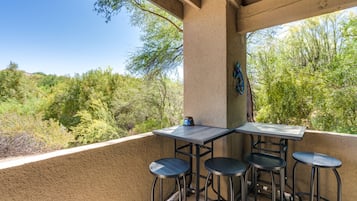 Une terrasse extérieure avec une table et quatre tabourets, entourée d’un mur de couleur beige et donnant sur une zone boisée.