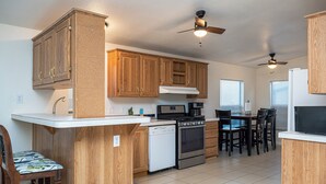 A kitchen with wooden cabinets, a dishwasher, a stove, and a dining area with chairs and a table.