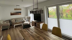 A modern living room with a wooden dining table, yellow chairs, a sofa set, and a television.