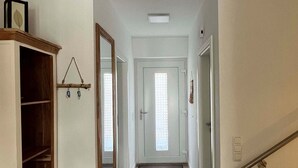 A hallway with a wooden floor, a door at the end, and a small wooden cabinet with a mirror.