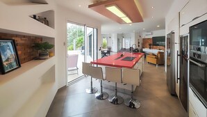 A modern kitchen with a central island, stainless steel appliances, and a large window providing natural light. - Nice home in Portiragnes (Portiragnes)