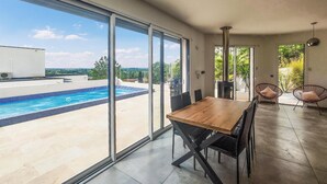 A modern dining area with a view of a swimming pool and a patio with chairs. - Nice home in Portiragnes (Portiragnes)