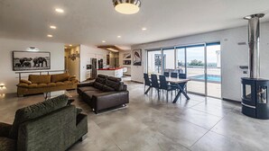 A modern living room with a sofa, a coffee table, and a fireplace. There is a dining area with a table and chairs. The room has large windows and a view of the outdoors. - Nice home in Portiragnes (Portiragnes)