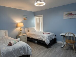 A bedroom with two beds, a desk, a chair, a lamp, and a window with blinds.