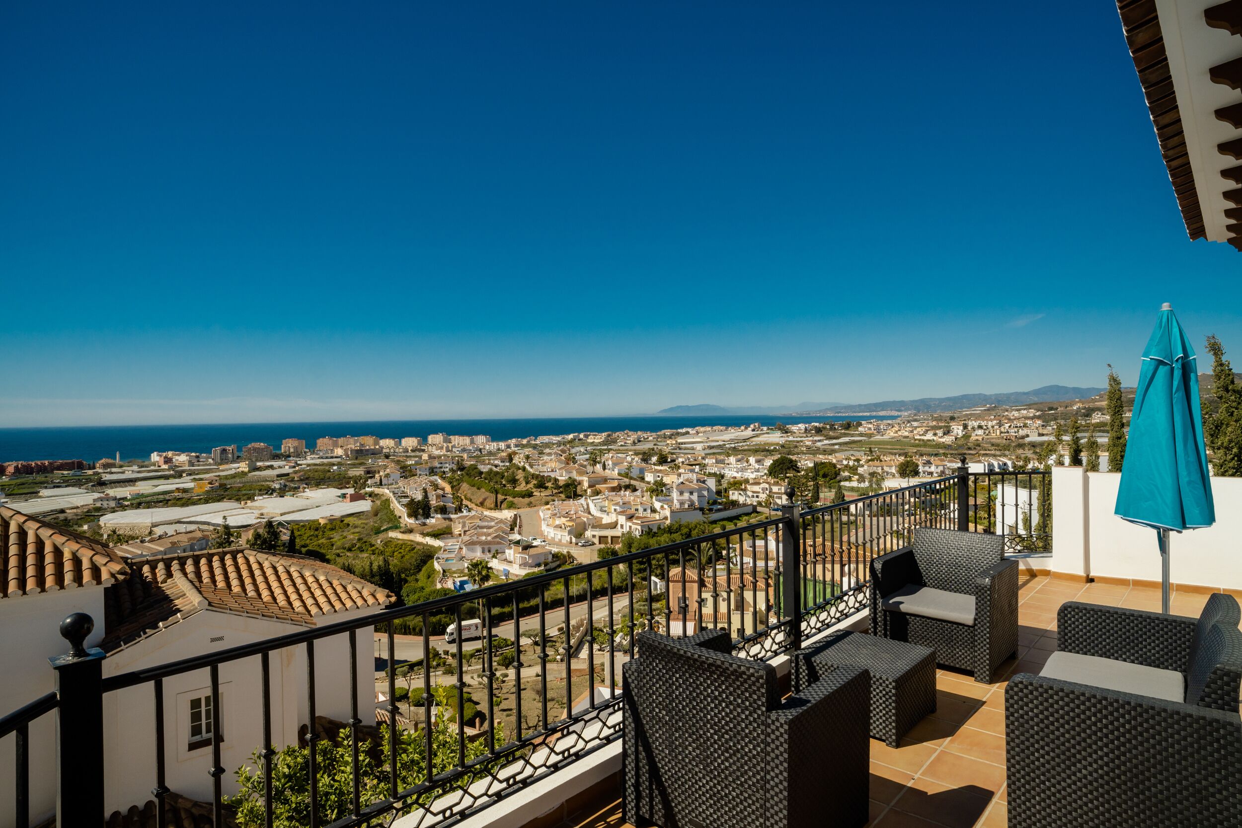 A balcony with wicker furniture and a view of a coastal cityscape.