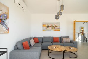 Een moderne woonkamer met een grijze modulaire bank, twee ronde salontafels en een stadsgezichtschilderij aan de muur.