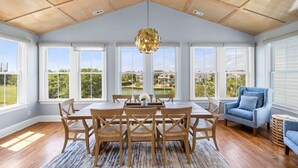 A spacious room with a high ceiling, large windows, a dining area with wooden furniture, and a view of a golf course.