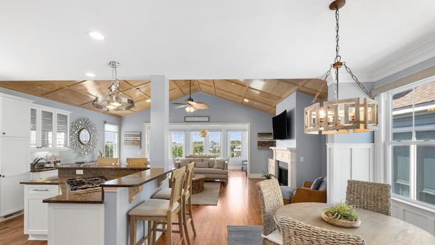 A spacious kitchen with a central island, wooden flooring, and a dining area with wicker chairs.